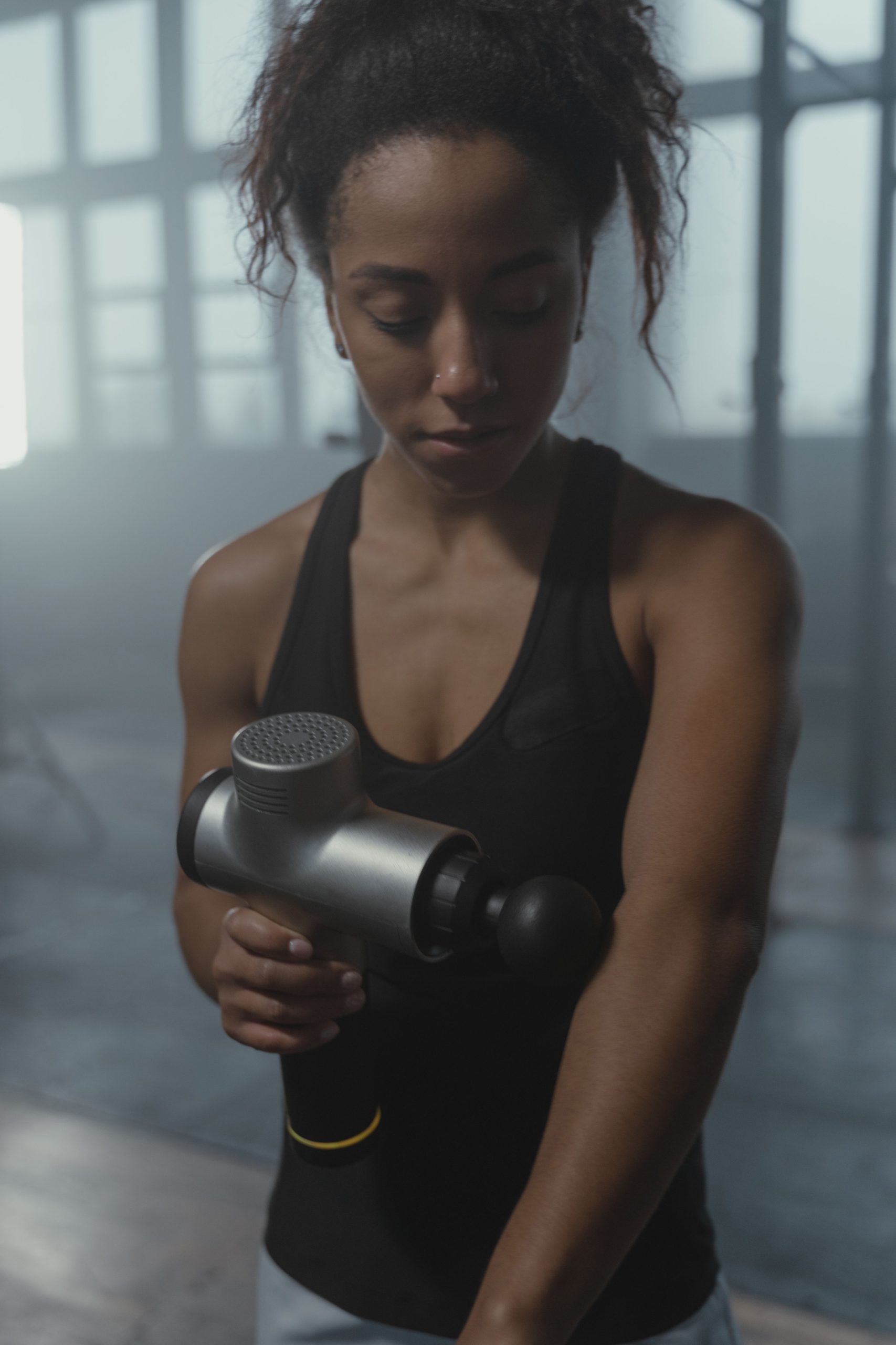 Woman using a percussion massage gun on her forearm
